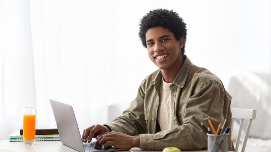 Home - Remote schooling concept. Black teen guy typing on laptop computer during his online studies at home